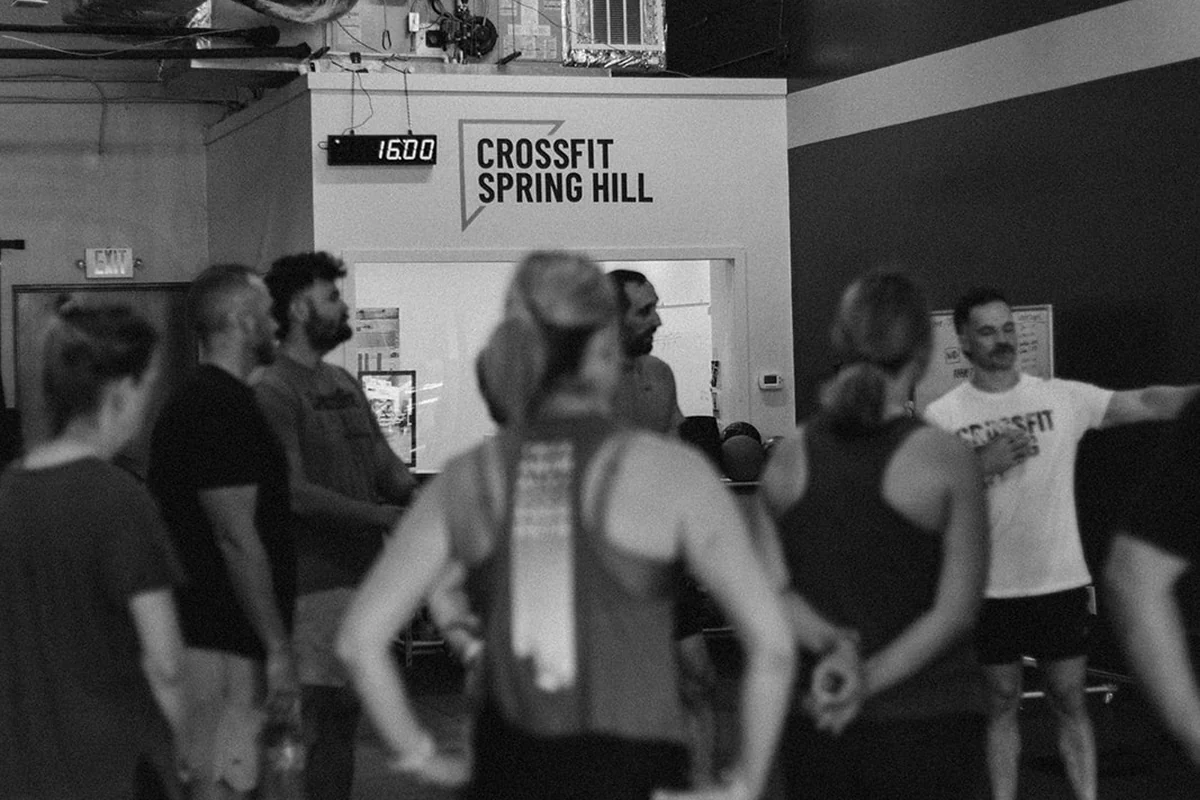 A CrossFit Spring Hill coach briefing a group class at the whiteboard before the workout starts