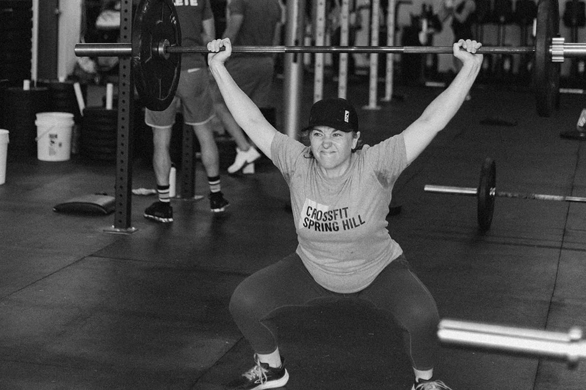 A CrossFit Spring Hill member in a gym shirt holding a barbell overhead at the bottom of a squat