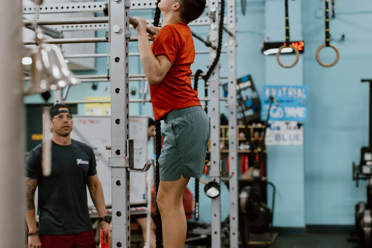 A teenager finishing a pull-up in the CrossFit Youth class at CrossFit Spring Hill while a coach watches
