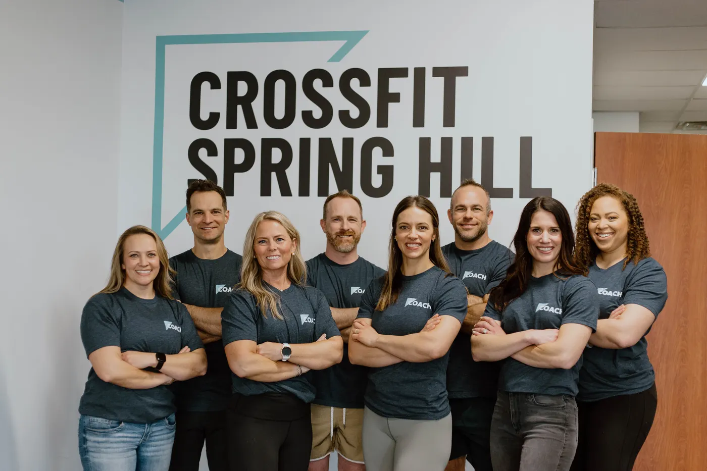 The CrossFit Spring Hill coaching team standing together in front of the gym logo wall in Spring Hill, TN