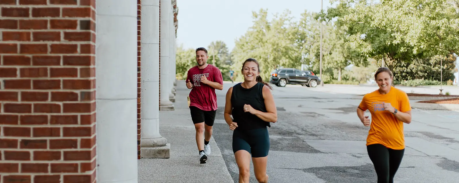 Three smiling CrossFit Spring Hill members running together outside the gym in Spring Hill, TN