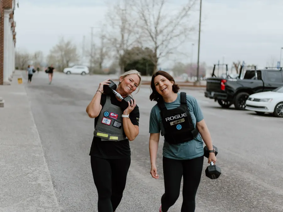 Two smiling CrossFit Spring Hill members carrying dumbbells in weight vests